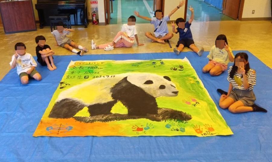 完成した等身大パンダの絵と一緒に笑顔で映る小学生達の様子