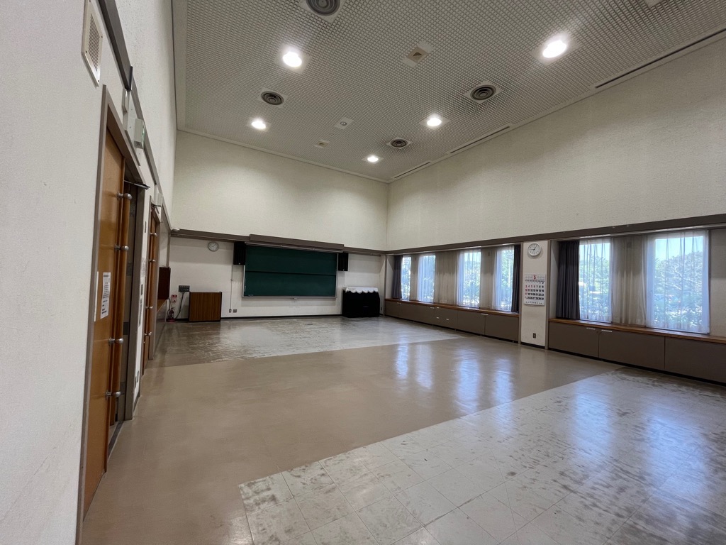 天井が高く、黒板とピアノが設備された広い集会室の写真
