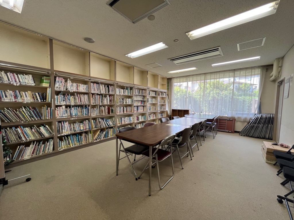 壁一面に本棚があり、真ん中に机と椅子が並べられた図書室の写真