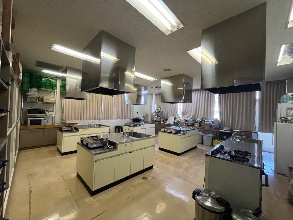 2口コンロ付きの調理台5台と調理器具が設備された調理室の写真