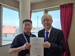 透き通るような青空が見える理事長室で、社会福祉法人柊の郷様と協定書を、社会福祉法人柊の郷理事長足高慶宣様（右側）、木更津市総務部前田部参事（左側）で持った記念写真。