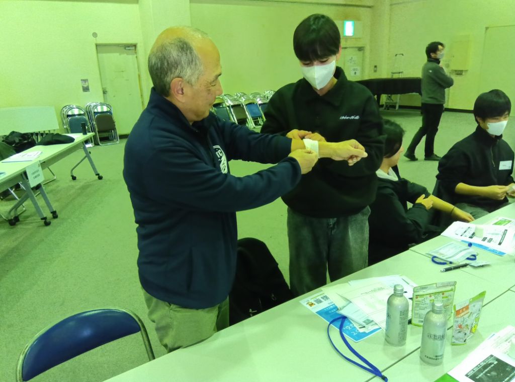 研修に参加した学生が、包帯を用いて応急手当の基礎を学んでいる様子です。