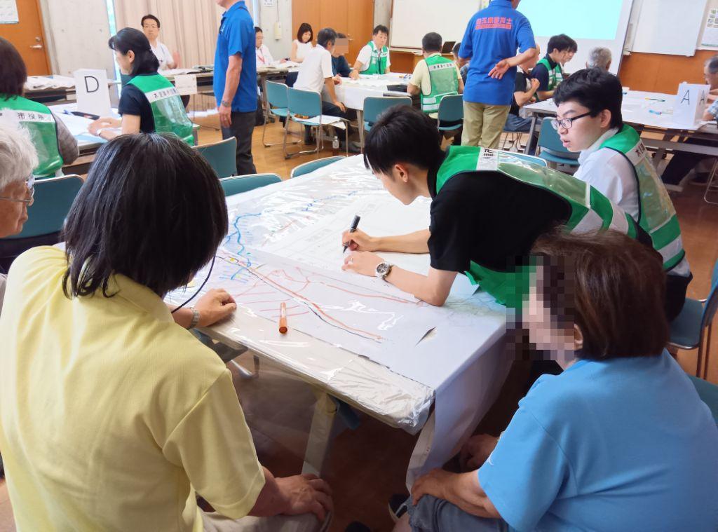 災害図上訓練（DIG）に取り組んでいる様子。机上に展開された白地図に、災害リスクや河川の位置などをマーカーで書き込んでいる様子。