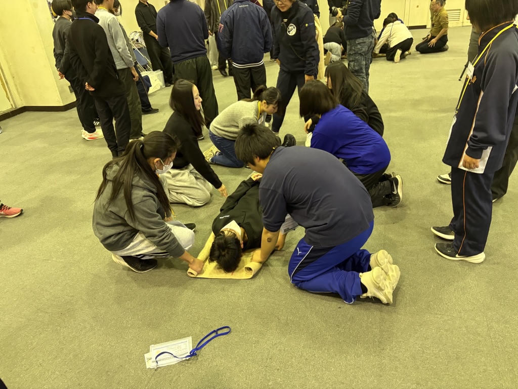 研修に参加した学生が、毛布を使用した負傷者の搬送方法について学んでいる様子です。