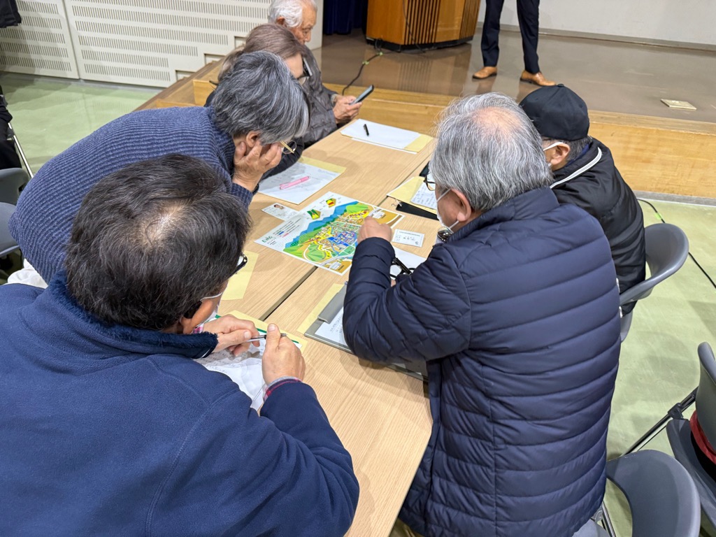 カードゲームタイプの防災教育教材を用いて、災害時の避難行動を疑似体験できるワークショップで、災害時にどこへ避難するかを考えている参加者の様子になります。